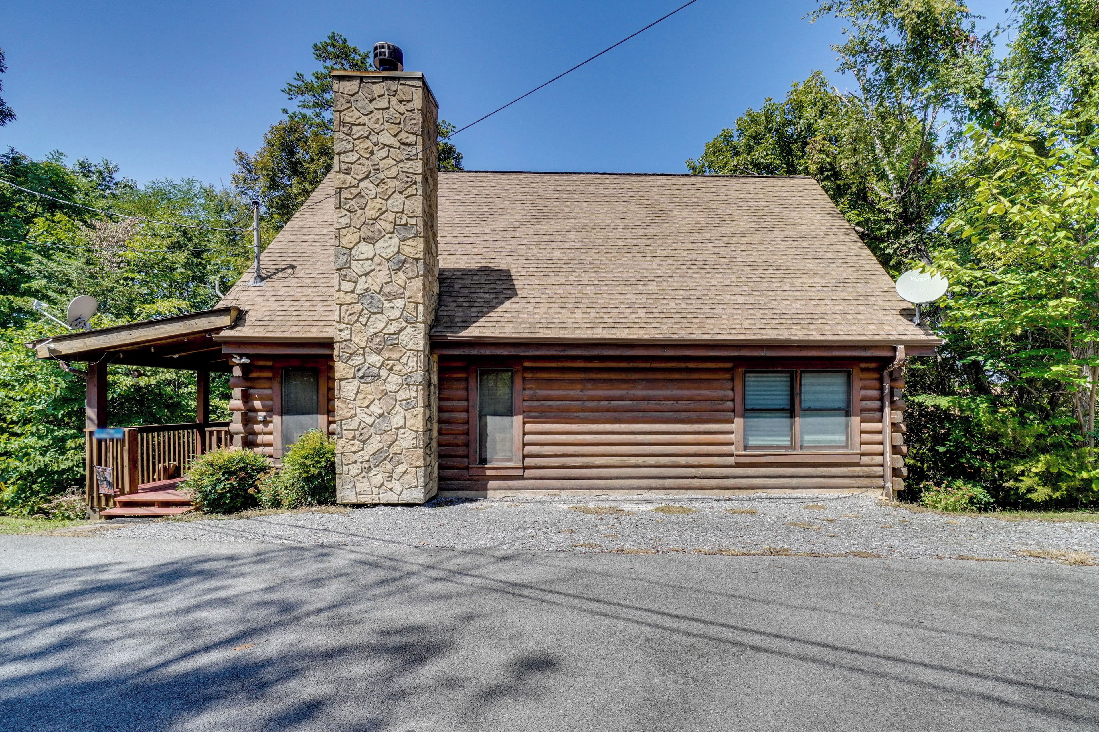A log cabin with a stone chimney, a covered porch, and a garage.