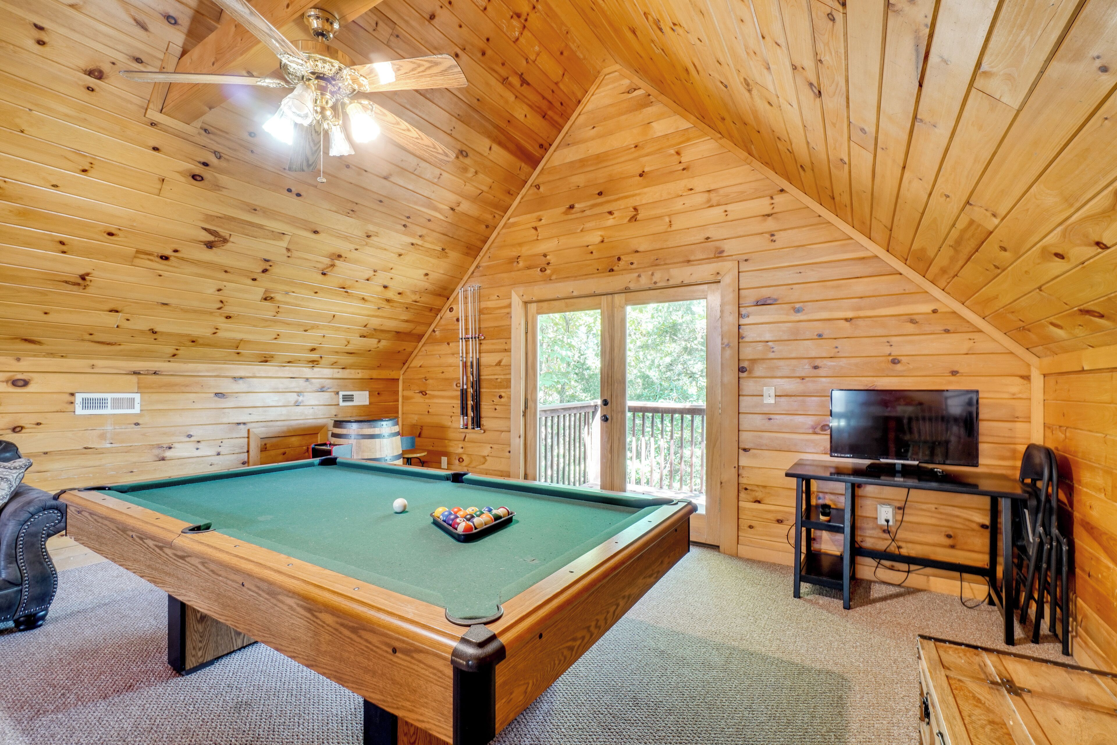 A wooden cabin with a pool table, a television, and a balcony.