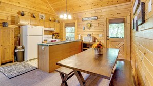 Cocina de cabaña de madera con una isla central, armarios de madera, un refrigerador, un microondas y un letrero que dice 'KITCHENS TOGETHER'.