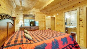 Un dormitorio de cabaña de madera con cama, cómoda, televisor y baño.