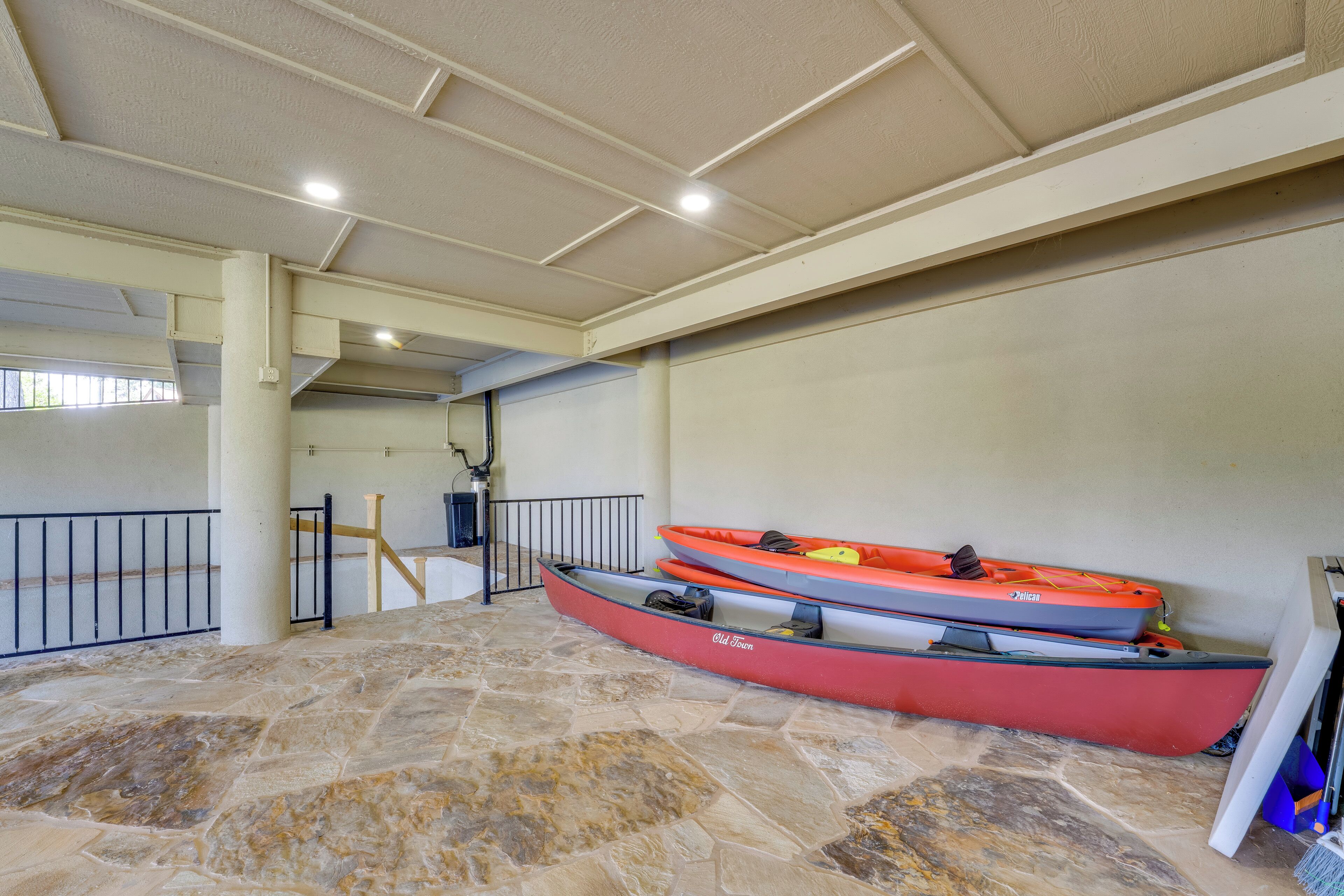Un espacio interior con piso de piedra, dos kayaks apoyados en una pared, una escalera y una barandilla.