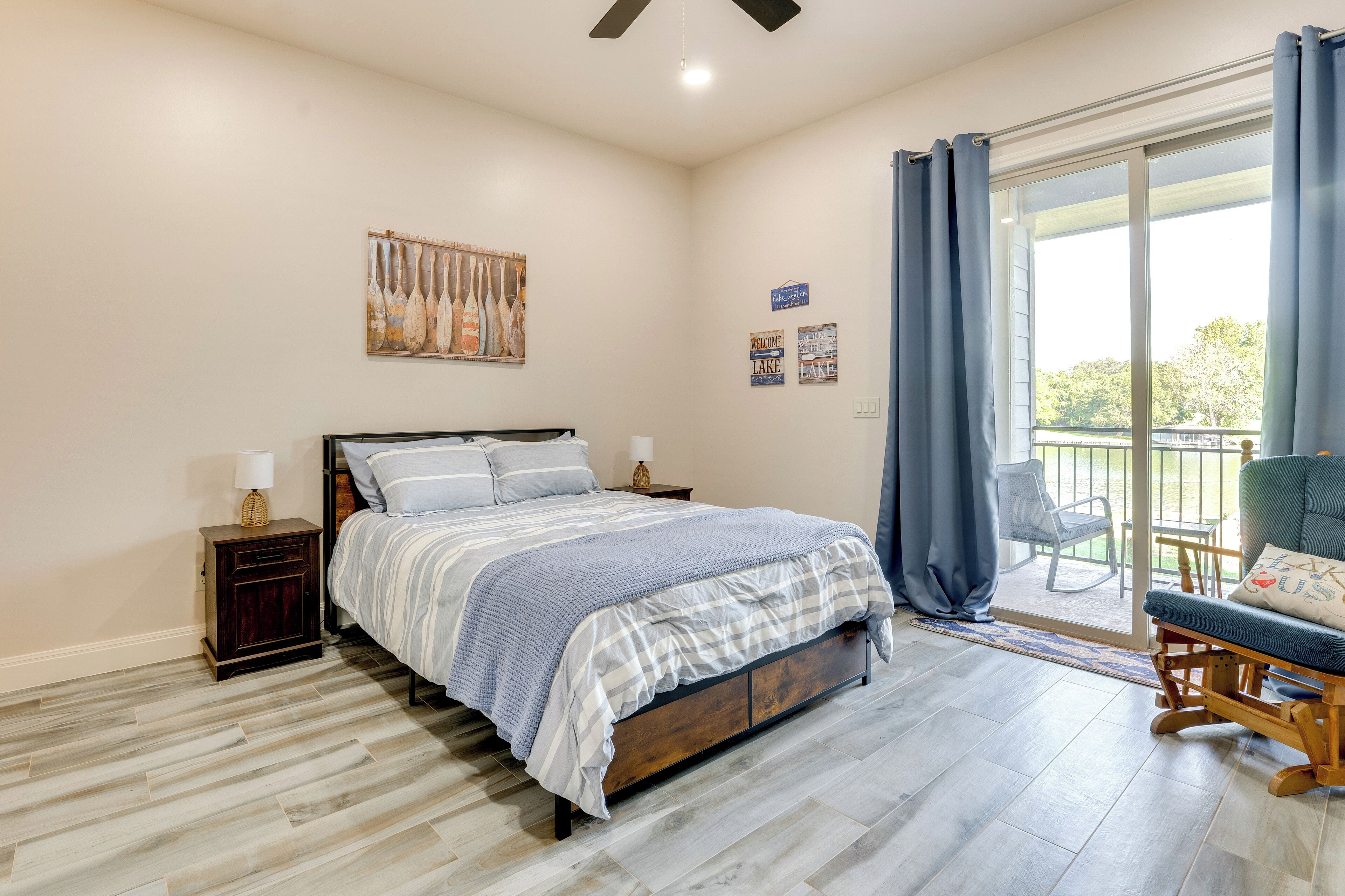 A bedroom with a bed, nightstands, a chair, and a view of the outdoors.