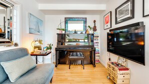 A compact living space with a piano, a sofa, a television, and a bookshelf. - Trail Access, Hot Tub: Lakefront Boulder Retreat! (Boulder)