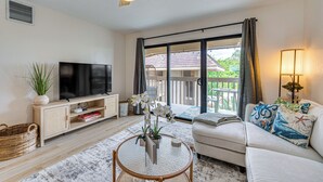 A living room with a television, sofa, coffee table, and a view of the outdoors. - Top Floor Ocean-view Condo: Walk to Kona Beaches! (Kailua-Kona)