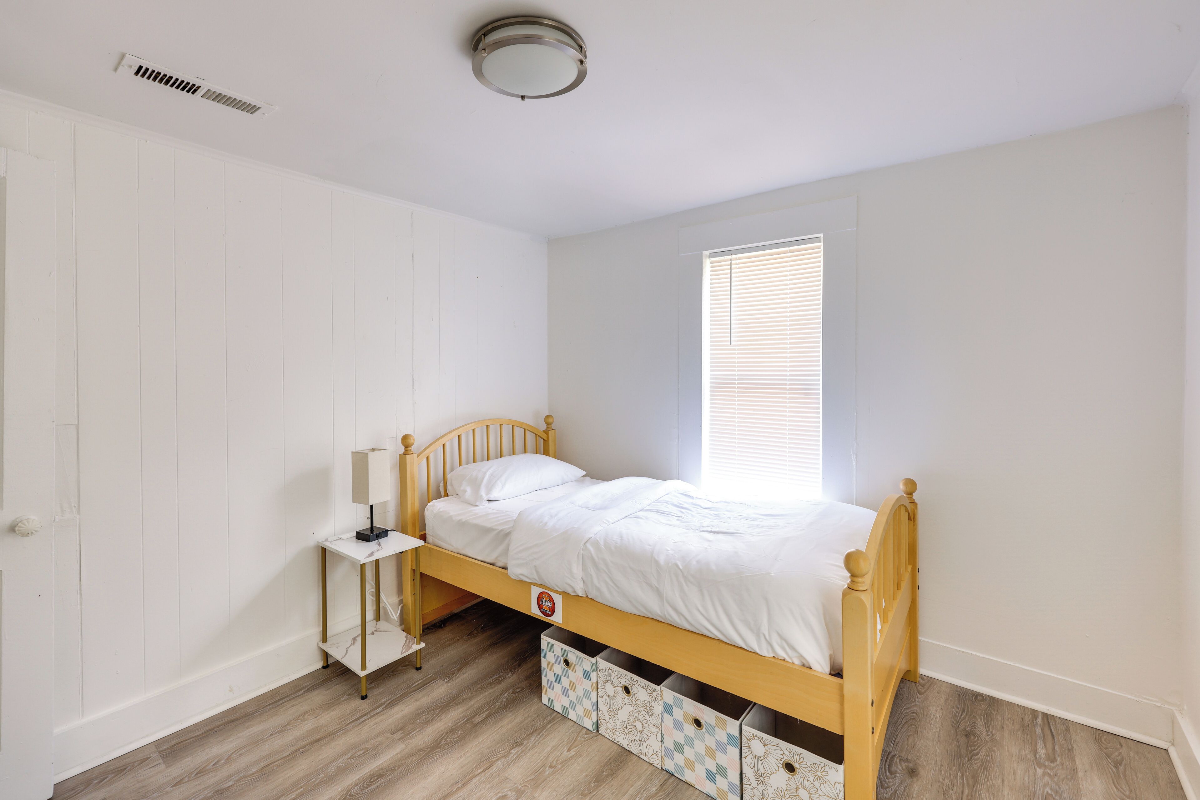 A bedroom with a wooden bed, a bedside table with a lamp, and storage drawers under the bed.