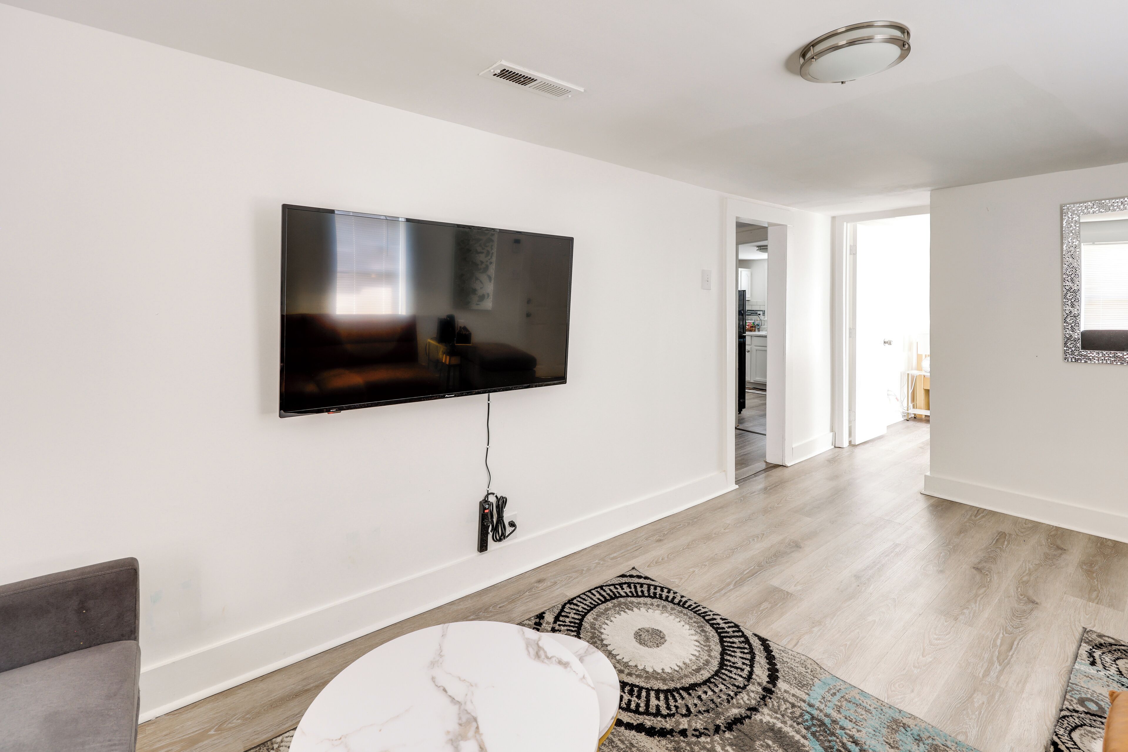 Una sala de estar moderna con un televisor de pantalla plana montado en la pared, un sofá gris, una mesa de centro de mármol blanco y una alfombra estampada.