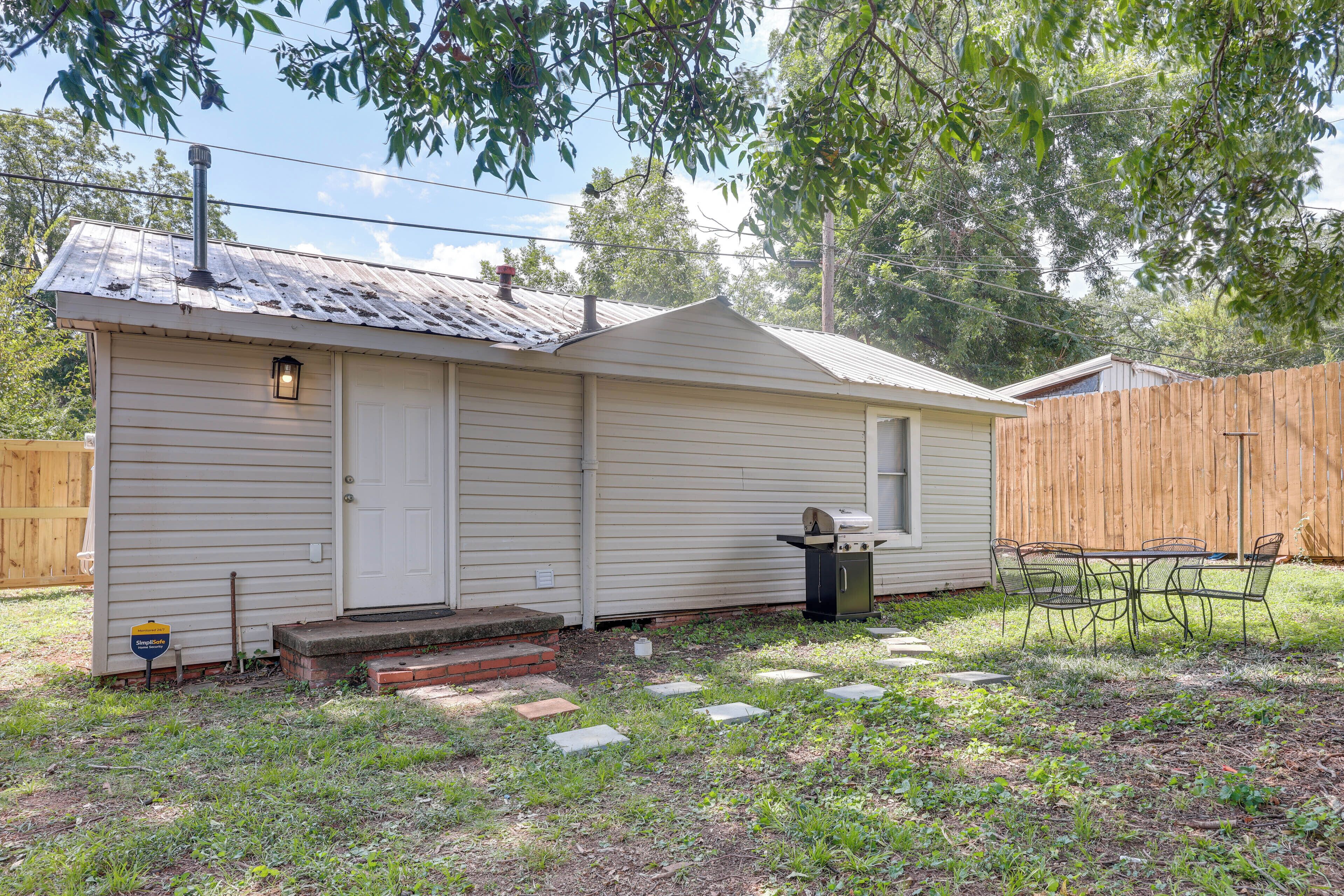 A single-story house with a front porch, a small attached garage, and a backyard with a wooden fence and a table with chairs.
