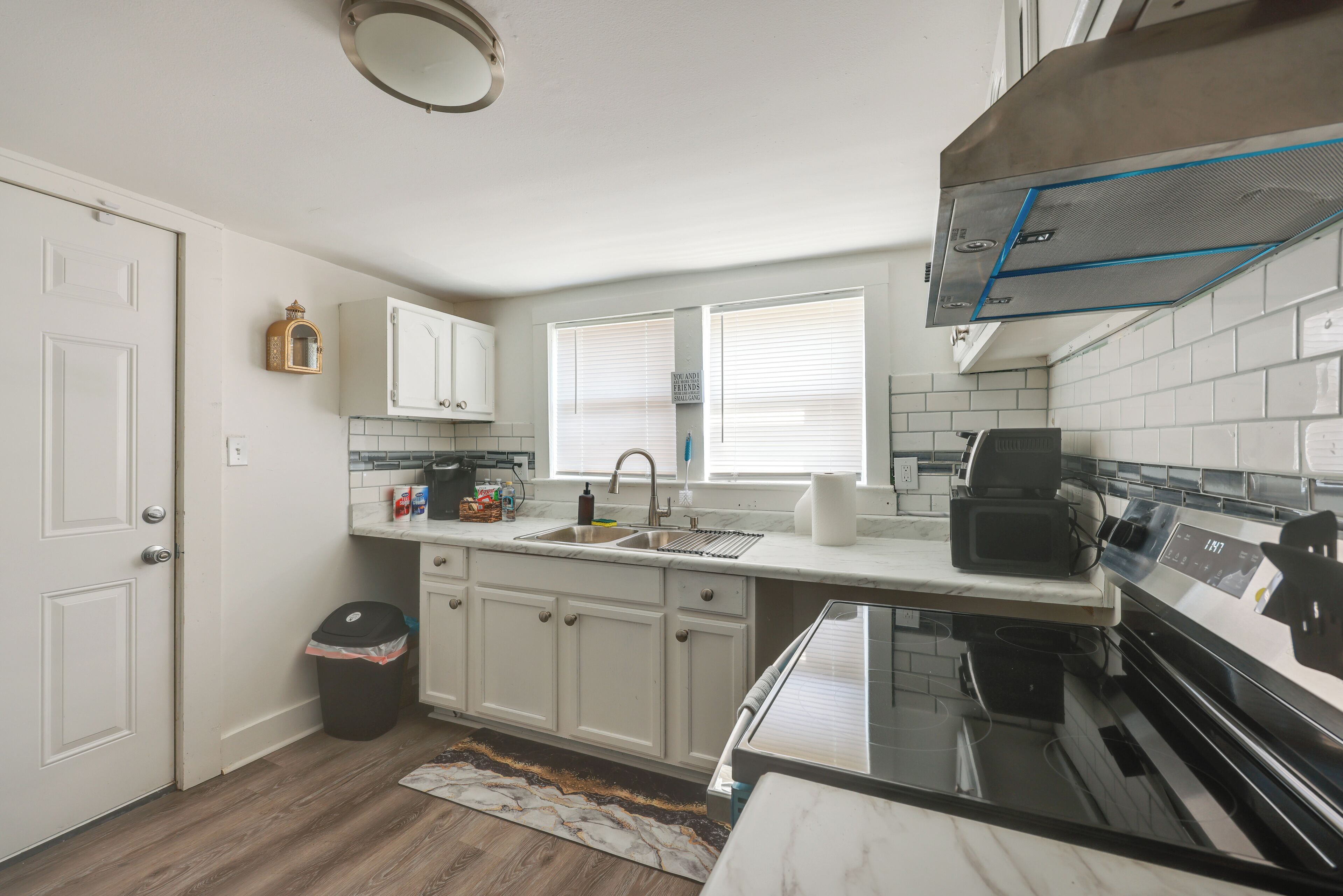 A kitchen with white cabinets, a stainless steel range hood, a microwave, and a sink.