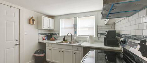 A kitchen with white cabinets, a stainless steel range hood, a microwave, and a sink.