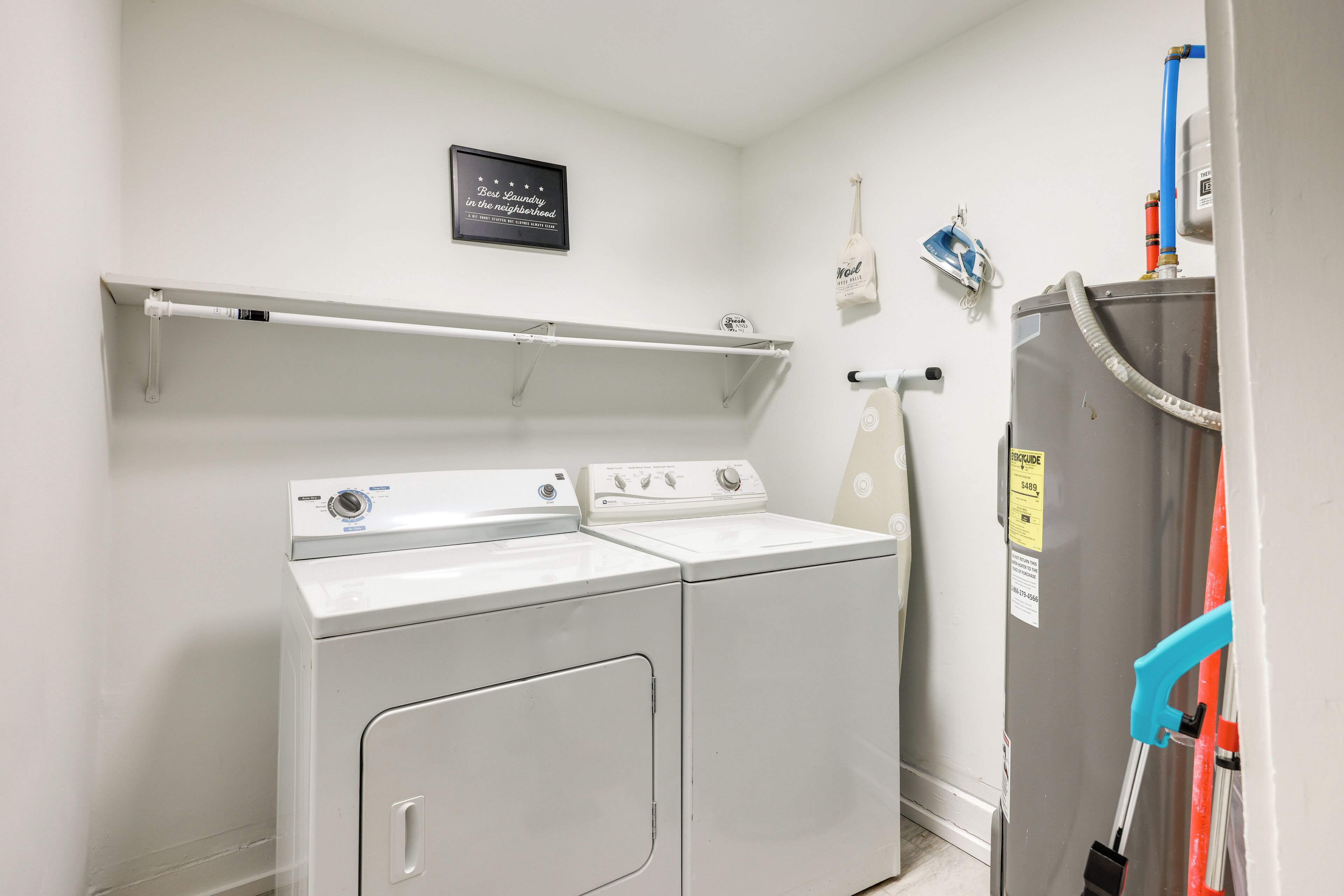 A laundry room with a front-loading washer and dryer, a shelf above the dryer, and a water heater on the wall.