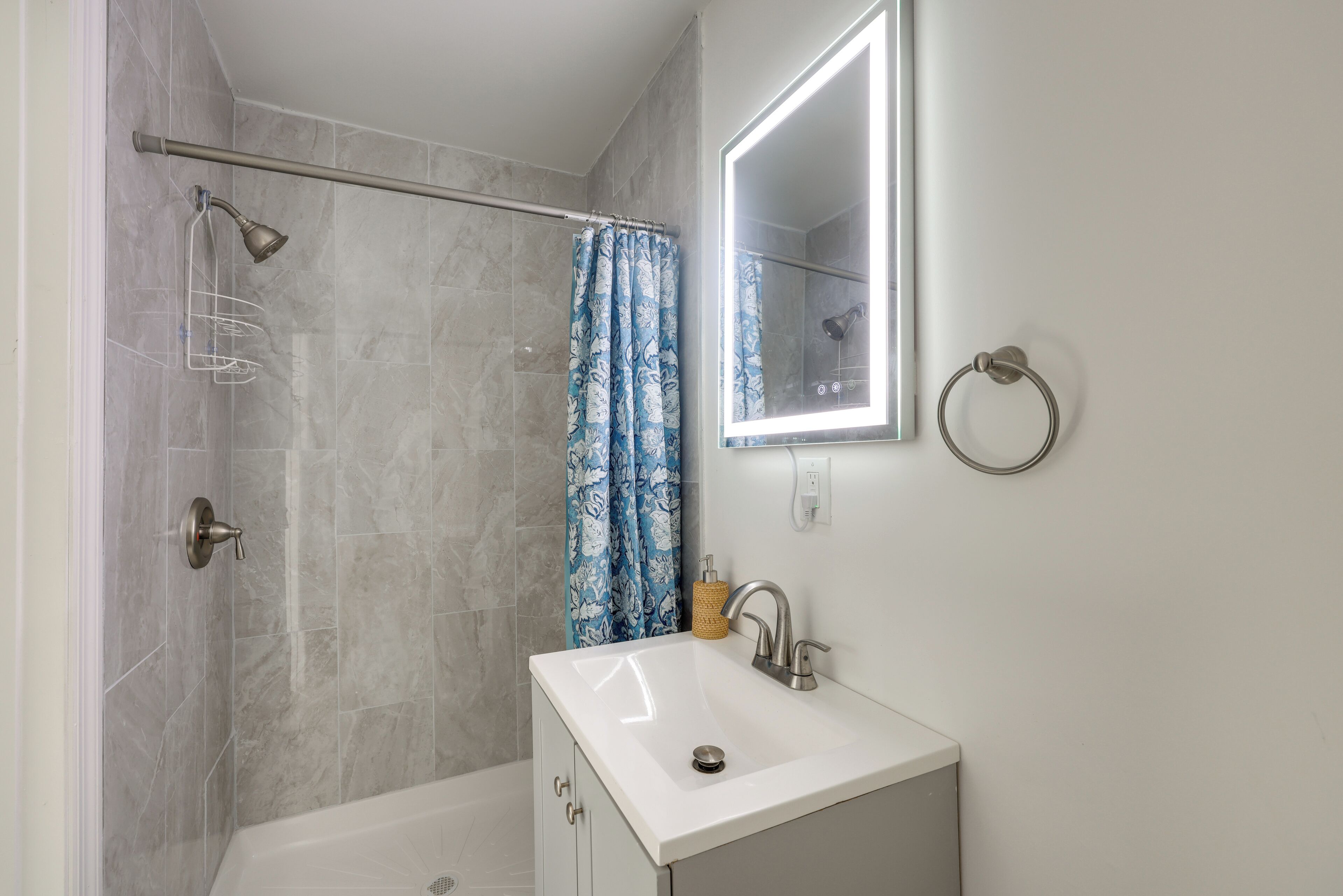 A bathroom with a shower, a sink, a mirror, and a towel ring.