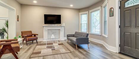 A spacious living room with a fireplace, a television mounted above it, and a large door with a decorative glass panel.