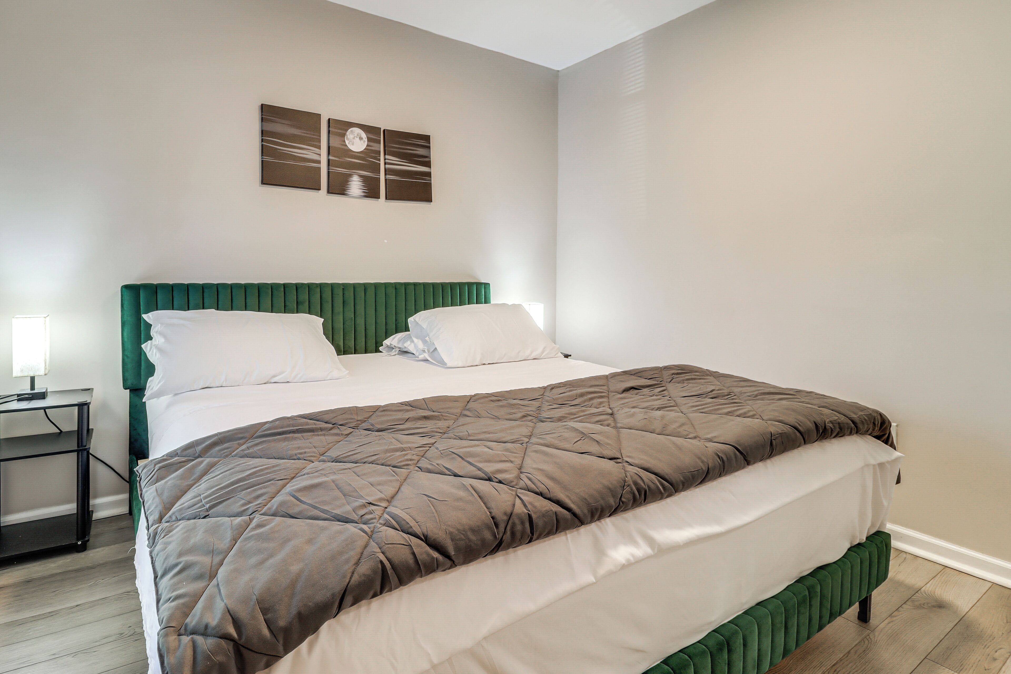 A neatly made bed with a green headboard, white pillows, and a brown quilt. There are two wall-mounted picture frames above the bed.