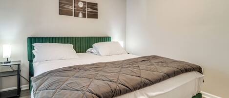 A neatly made bed with a green headboard, white pillows, and a brown quilt. There are two wall-mounted picture frames above the bed.
