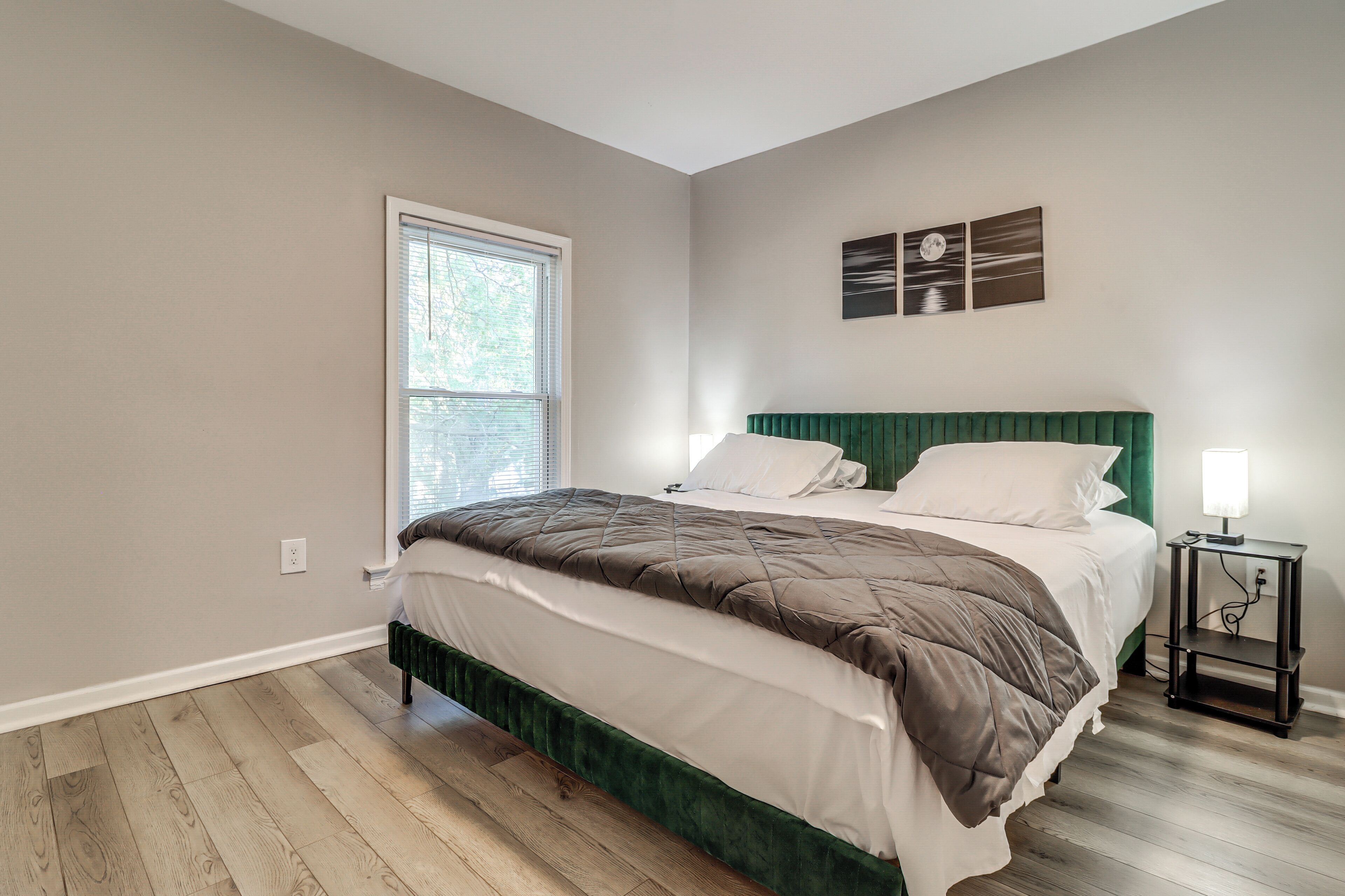 A bedroom with a bed, a window, a nightstand, and a wall-mounted light fixture.