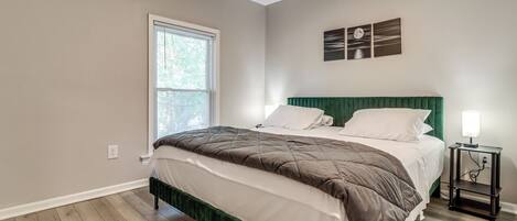 A bedroom with a bed, a window, a nightstand, and a wall-mounted light fixture.
