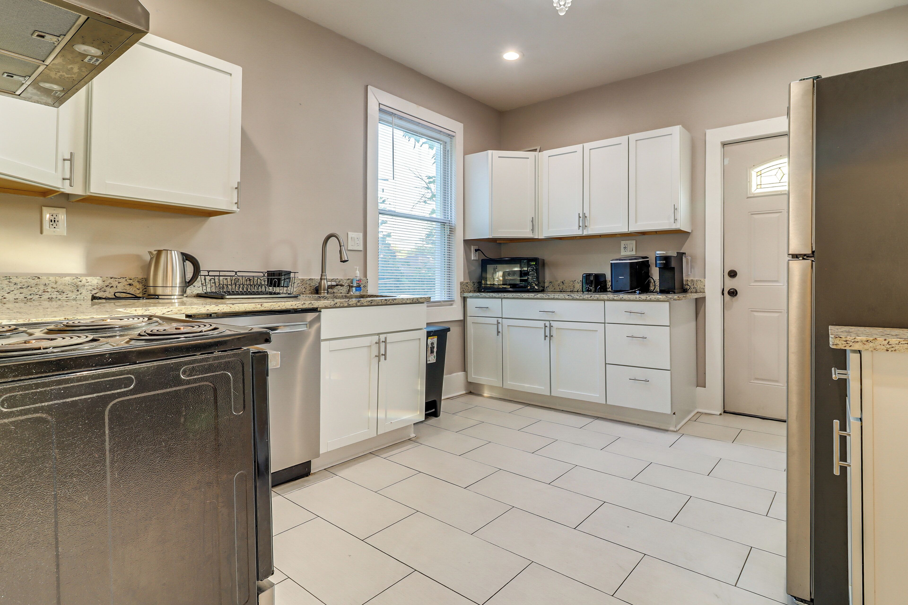 A modern kitchen with white cabinets, stainless steel appliances, and a tiled floor.