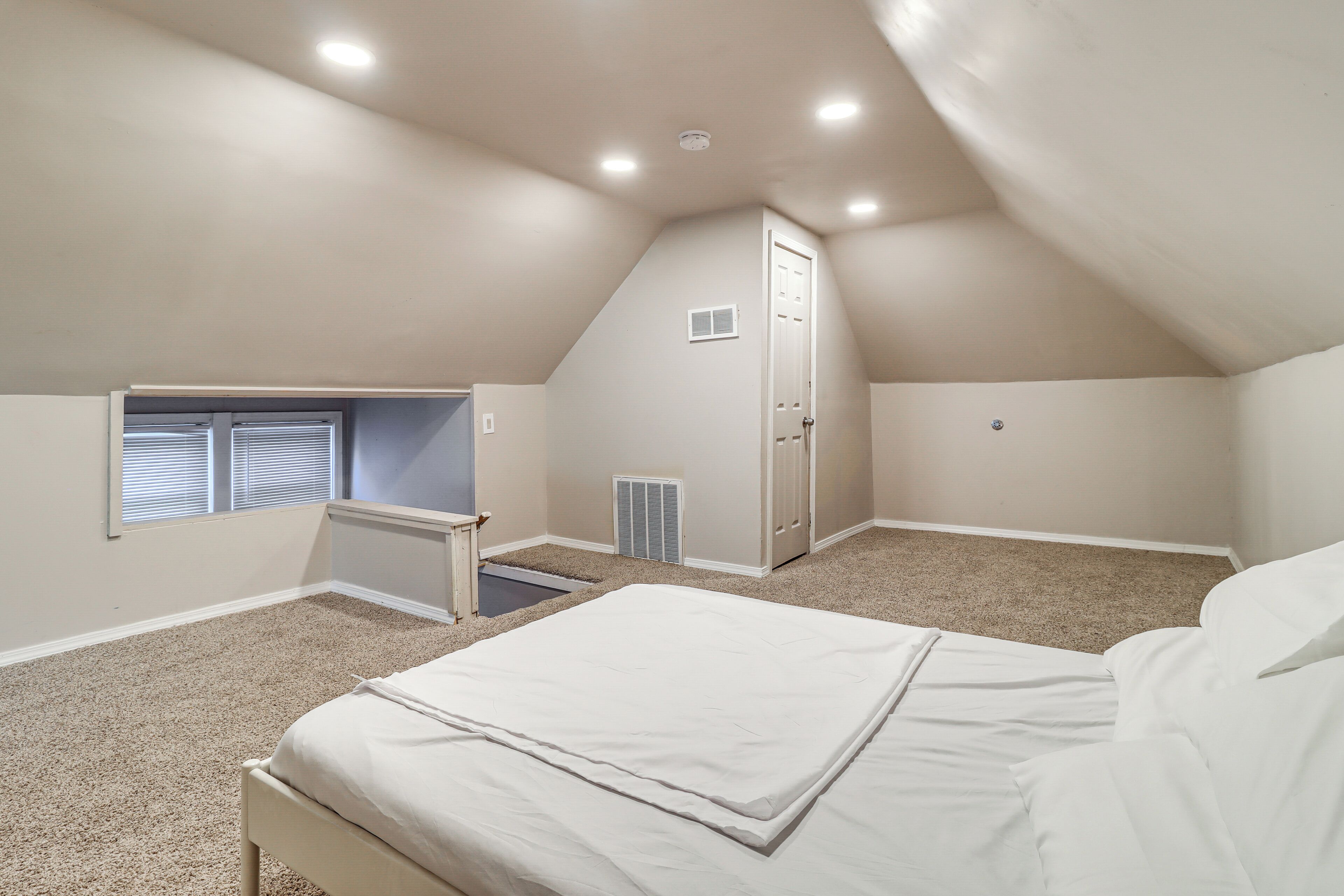 A bedroom with a sloped ceiling, a bed, a window, a door, and a radiator.