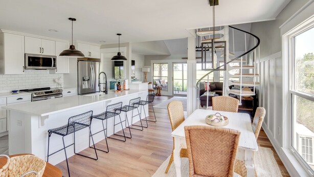Cocina moderna con armarios blancos, una isla central con taburetes y un refrigerador de acero inoxidable, además de un microondas integrado.