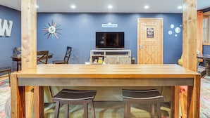Uma área de bar com madeira, uma TV, cadeiras de madeira e um letreiro com a inscrição 'WHITECAP MOUNTAINS'.