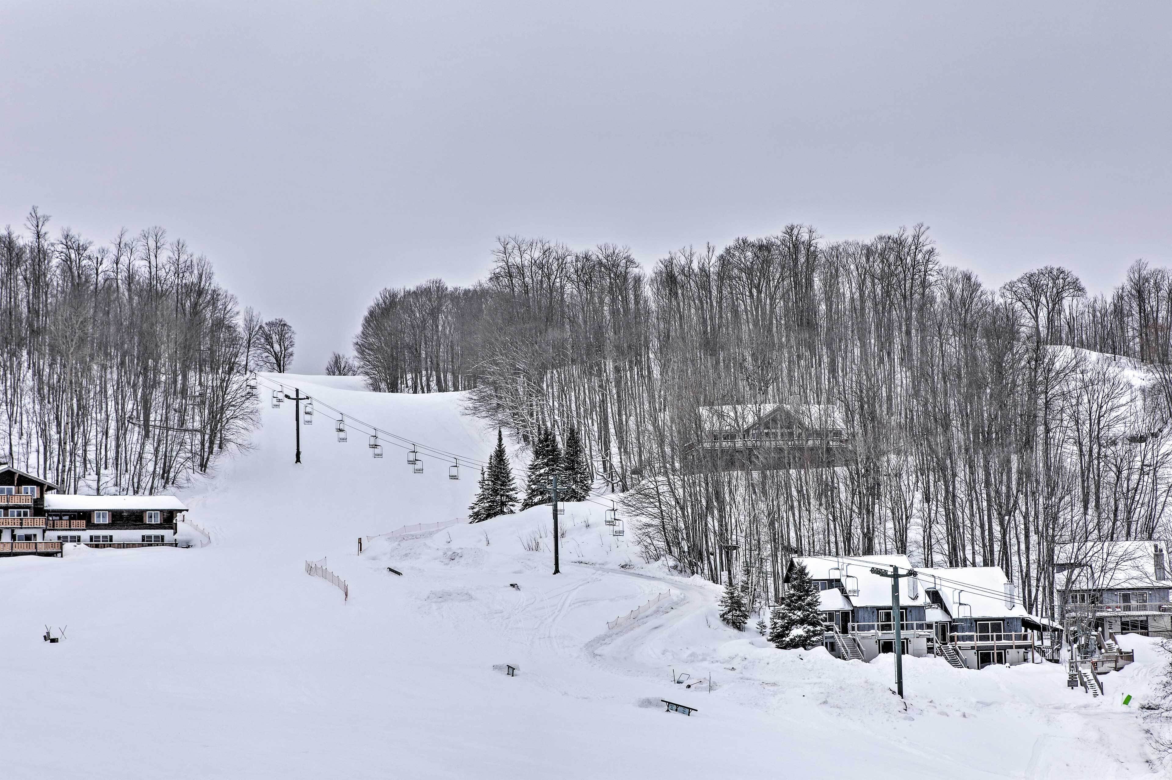 A snow-covered ski resort with buildings, ski lifts, and a forested mountain backdrop.