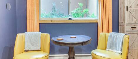 A room with two yellow chairs, a small round table, a window with curtains, and a wooden cabinet.