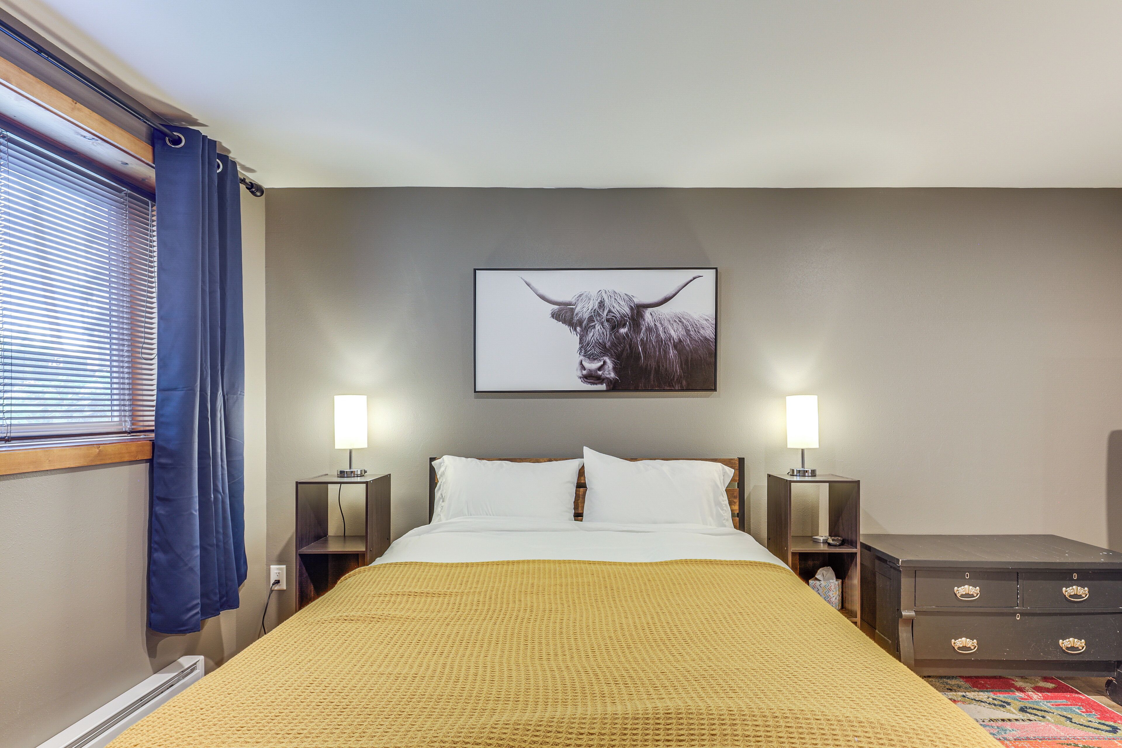 A bedroom with a bed, two bedside tables, a lamp, a dresser, and a framed picture on the wall.