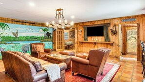 A cozy living room with leather sofas, a chandelier, a mural, and a wooden wall. - Sandy Shore & Multi-boat Dock! St Johns River Home (Astor)