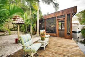 A wooden deck with outdoor furniture, a large window, and a boat in the background.