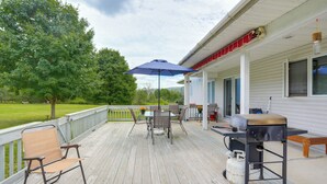 Une terrasse couverte équipée d’un barbecue, d’une table d’extérieur, de chaises et d’un parasol bleu.