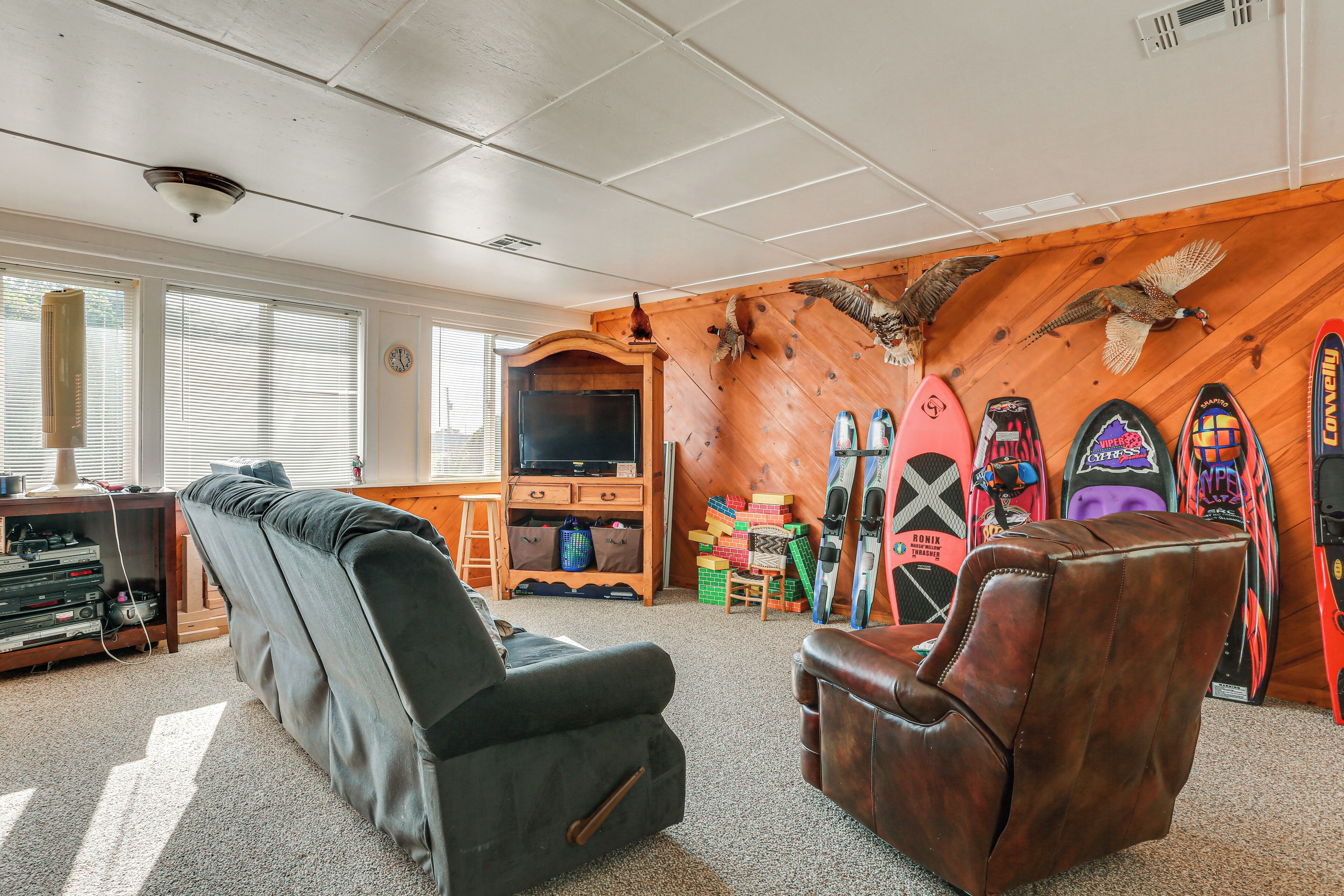 Ein Wohnzimmer mit einer Couch, einem Ledersessel, einem Fernseher, einer Holzwand mit angebrachten Skiern und einem Kamin.
