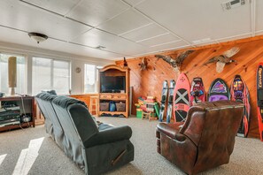 Un salon comprenant un canapé, un fauteuil en cuir, un téléviseur, un mur en bois orné de paires de skis et une cheminée.