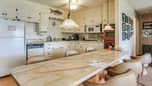 Una cocina con encimera de mármol, armarios blancos y zona de comedor con sillas.