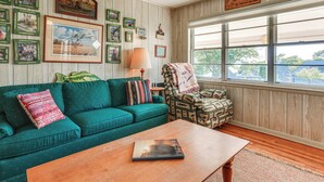 Una sala de estar acogedora con un sofá color turquesa, un sillón estampado, una mesa de centro de madera y un ventanal con vistas al exterior.