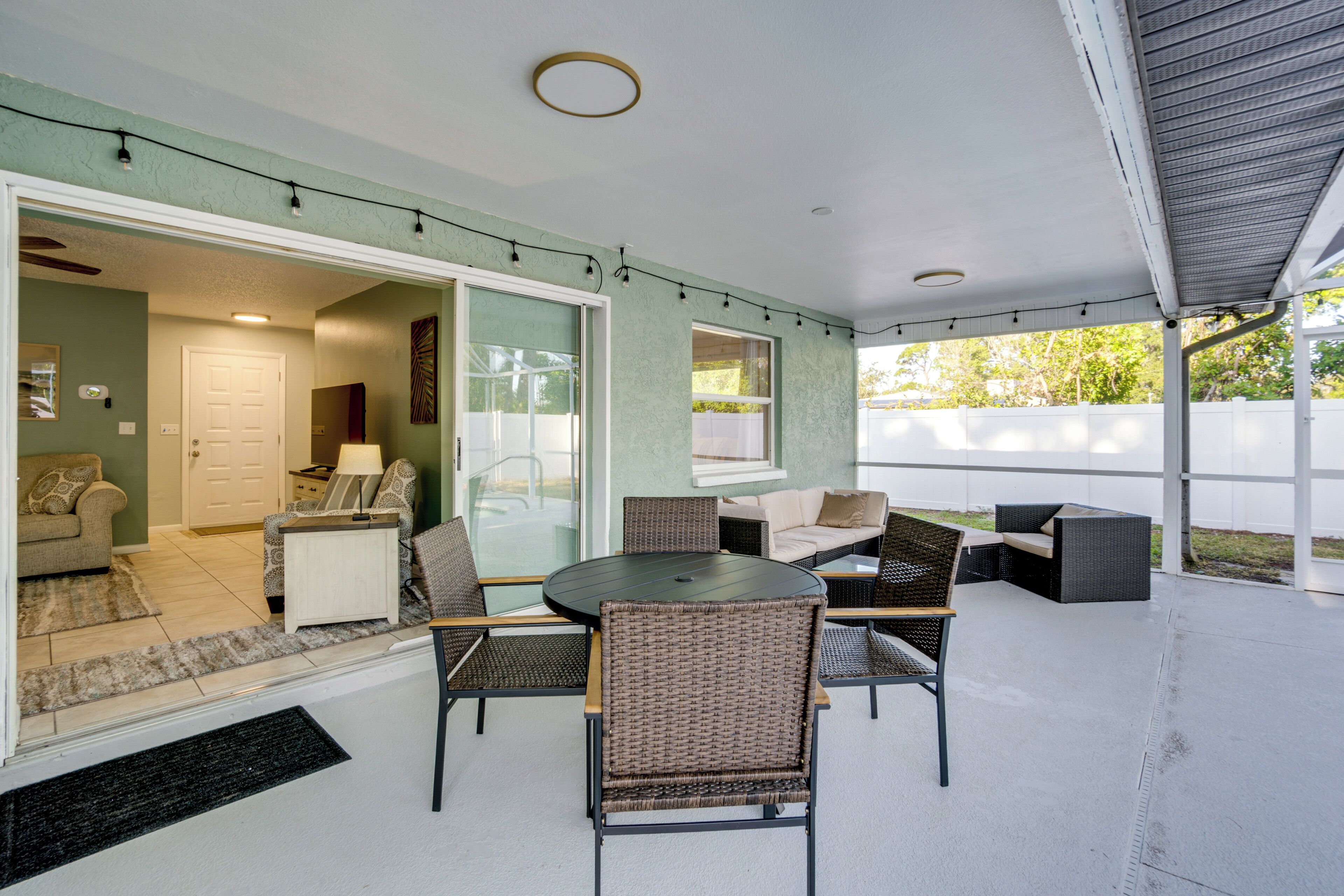 An outdoor patio with a round table and wicker chairs, a sofa, and a glass door leading to an indoor living area.