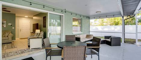 An outdoor patio with a round table and wicker chairs, a sofa, and a glass door leading to an indoor living area.
