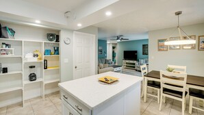 A modern kitchen with white cabinetry, a central island, and a dining area with a wooden table and chairs. - 3 Mi to Manasota Key: Stylish Single-story Home! (Venice)