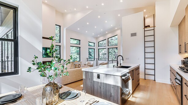 A modern kitchen with a central island, large windows, and a dining area set up for a meal. - 4 Mi to Soda Springs Resort: Hot Tub Hideaway! (Truckee)