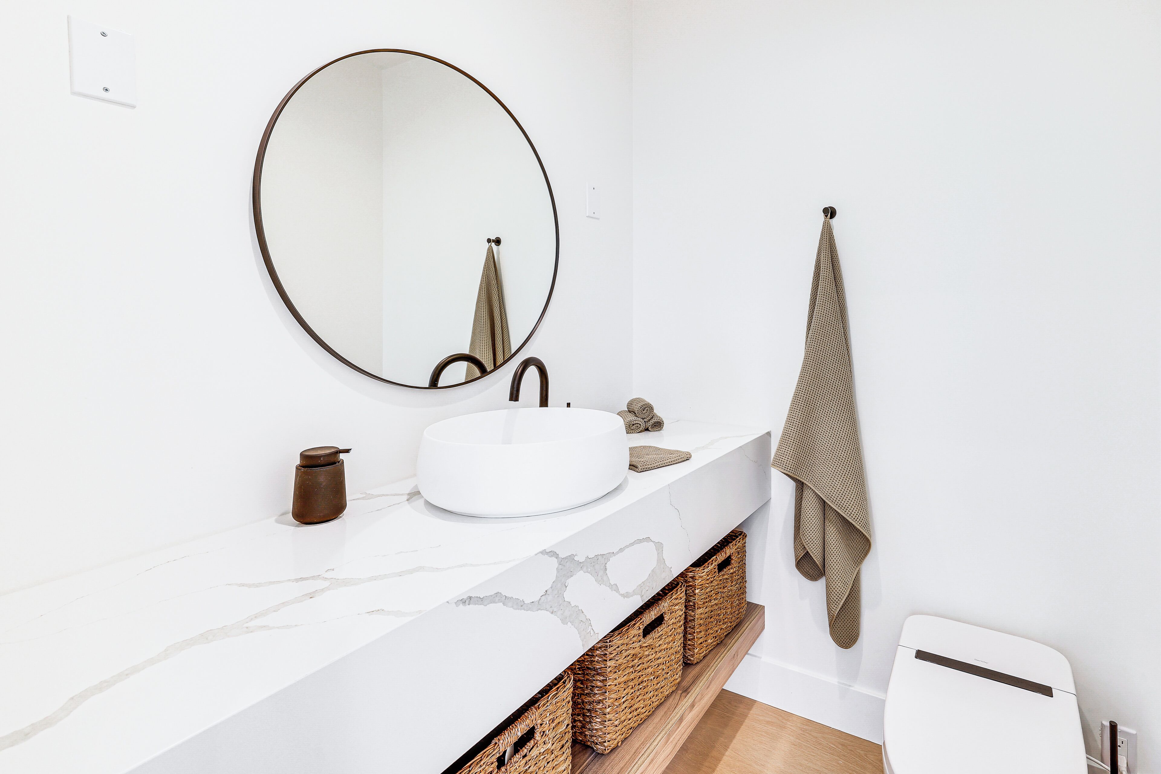 A modern bathroom with a white marble sink, a round mirror, and a towel hanging on a hook.