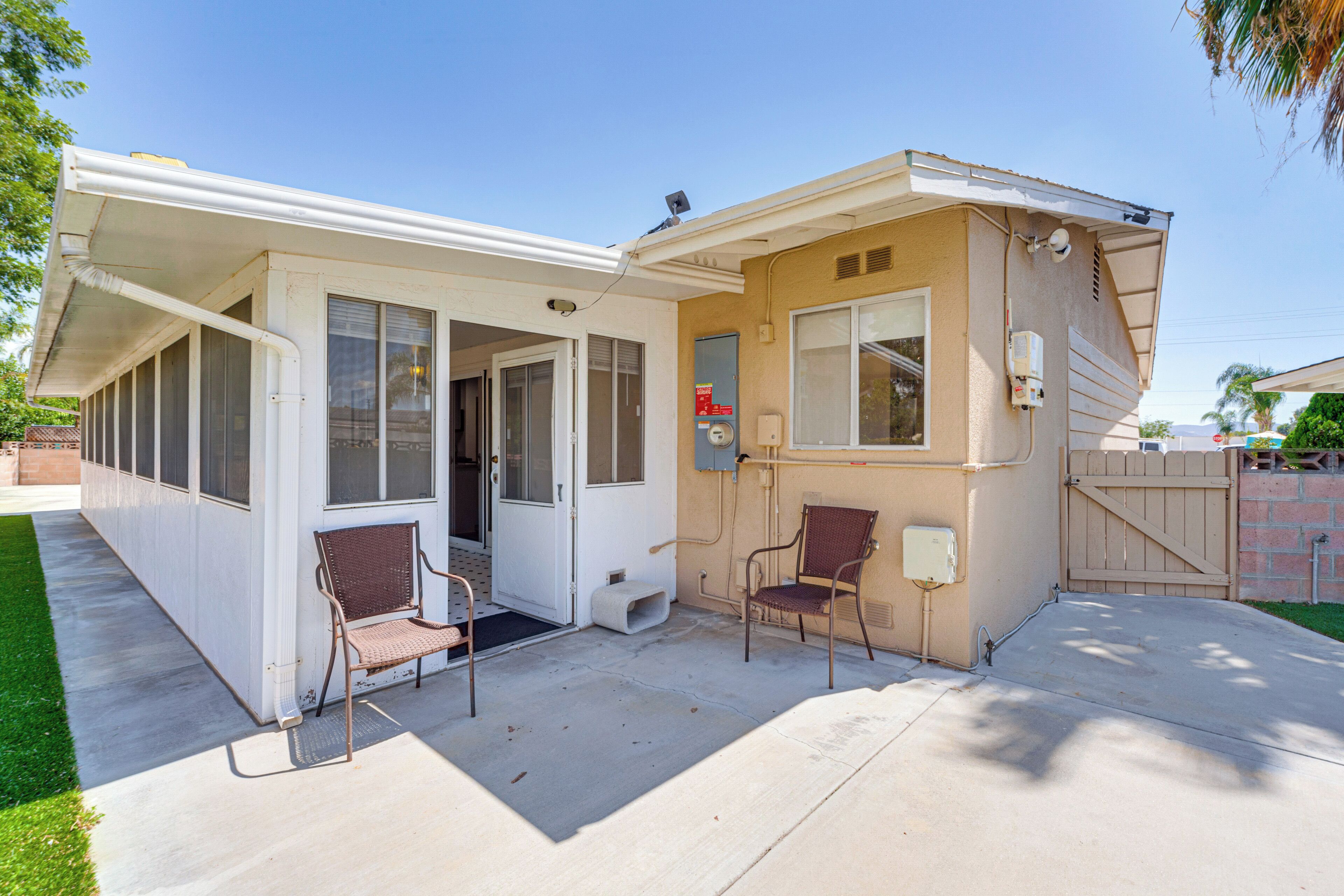 A single-story house with a covered patio, two chairs, a small porch, and a gated entrance.