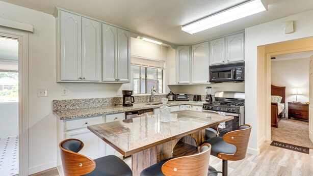 A modern kitchen with granite countertops, white cabinets, a central island with bar stools, and a microwave above the stove. - Hemet Retreat w/ Peak Views + 2 Saunas (Hemet)