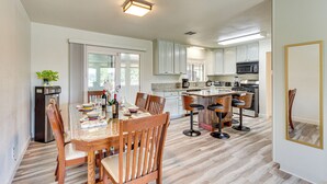A modern kitchen with white cabinets, a central island with bar stools, and a dining area with wooden chairs and a glass-top table. - Hemet Retreat w/ Peak Views + 2 Saunas (Hemet)