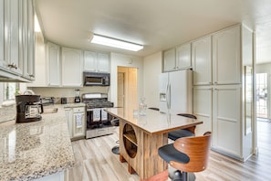 A modern kitchen with white cabinetry, a granite countertop, a central island with bar stools, and stainless steel appliances. - Hemet Retreat w/ Peak Views + 2 Saunas (Hemet)