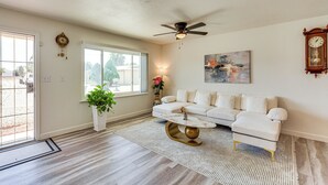 A living room with a white sofa, a coffee table, a ceiling fan, a clock, and a painting on the wall. - Hemet Retreat w/ Peak Views + 2 Saunas (Hemet)