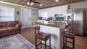 A kitchen with wooden ceiling, white cabinets, a stainless steel refrigerator, and a bar stool. - Private Dock: Des Allemands Cabin on the Bayou! (Des Allemands)