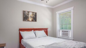 A bedroom with a wooden bed, a painting on the wall, and a window with blinds. - Private Dock: Des Allemands Cabin on the Bayou! (Des Allemands)