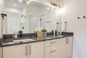 Ein modernes Badezimmer mit großem Spiegel, einer Arbeitsplatte aus Granit und hellen Holzschränken.