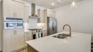 A modern kitchen with stainless steel appliances, white cabinetry, and a large island with a sink.
