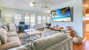 A living room with a large TV, a ceiling fan, and a view of the beach through the windows. - 'the Waterfront Cottage' w/ Dock in Goodland! (Goodland)
