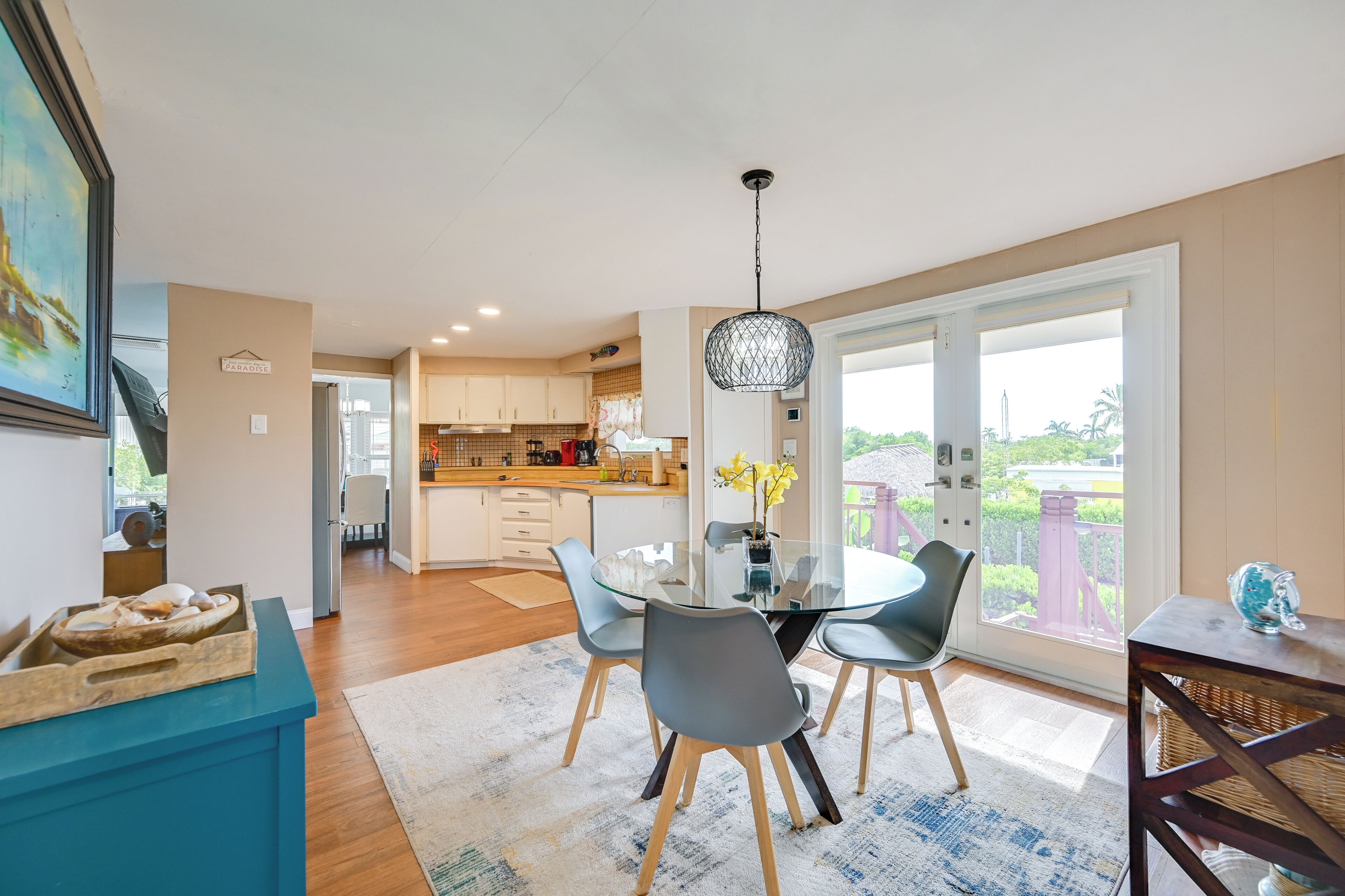A modern kitchen with a glass dining table, grey chairs, and a hanging light fixture.